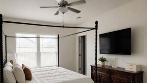 Un letto a baldacchino con ventilatore a soffitto, un televisore a parete e un armadietto in legno con cassetti.