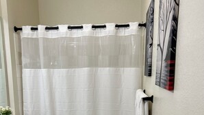 A bathroom with a shower curtain, toilet, rug, and a towel rack. - Bright apartment in a superb Virginia Beach location with AC (Virginia Beach)