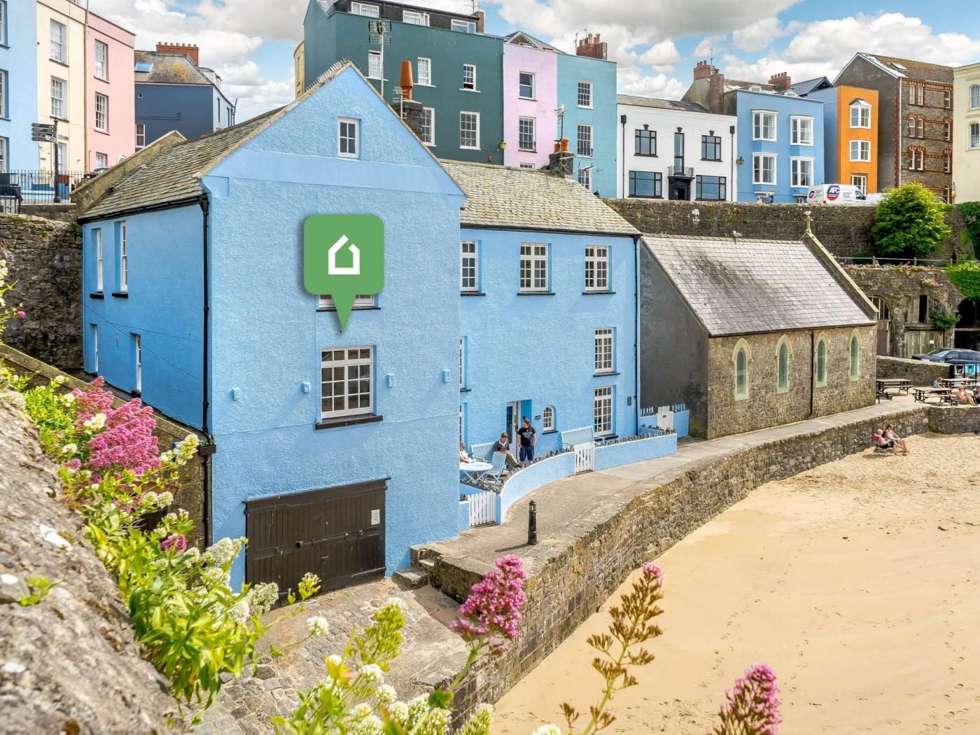 A coastal building with a prominent green speech bubble icon, a stone wall, and a sandy beach in the foreground.