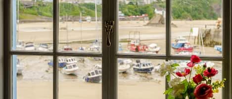 Una ventana con vistas a barcos en una orilla arenosa, un mecanismo de cierre y un florero con flores.