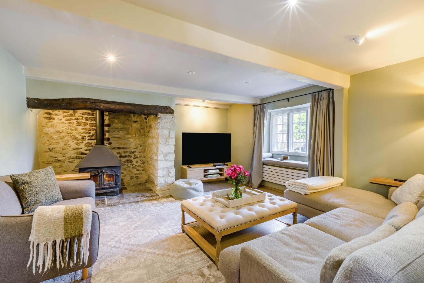 A cozy living room with a stone fireplace, a comfortable sofa set, a flat-screen TV, and a window with curtains.