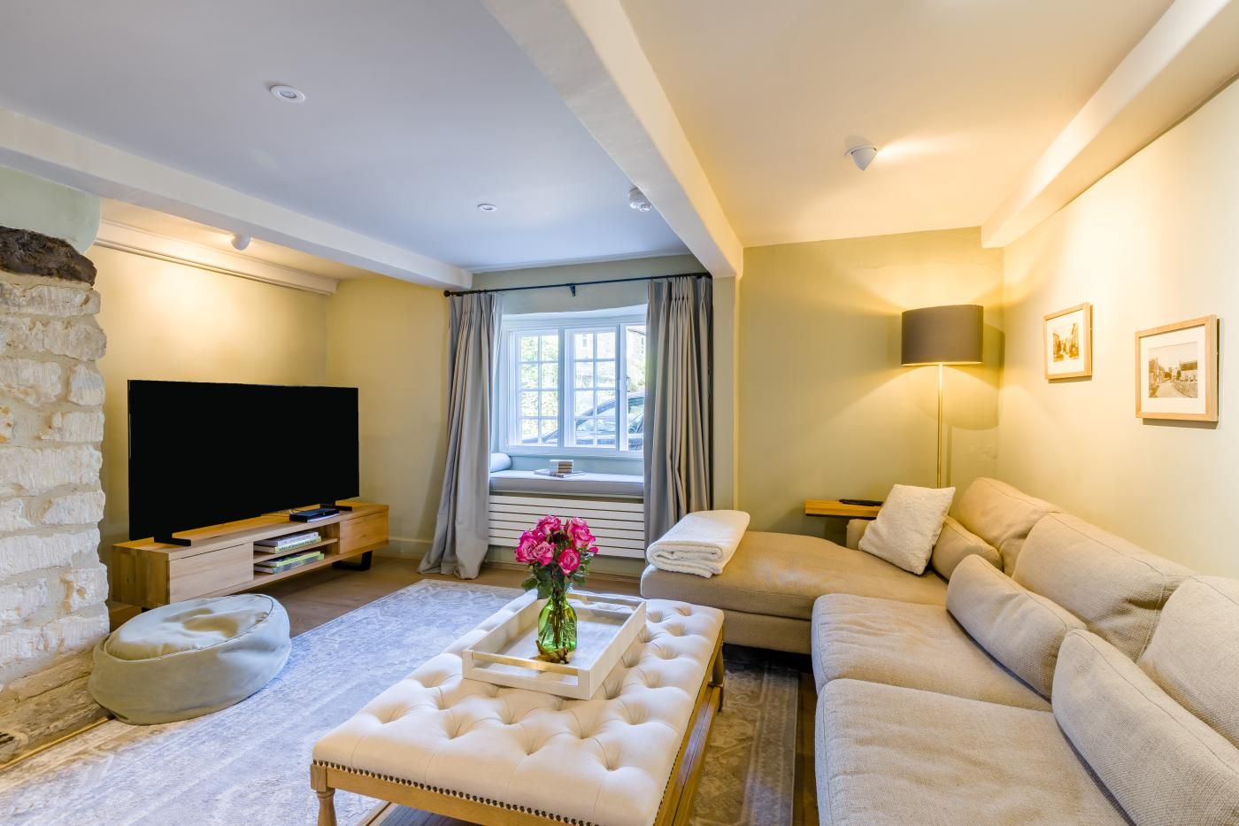 A modern living room with a flat-screen TV, a beige sofa, a white ottoman, and a stone accent wall.