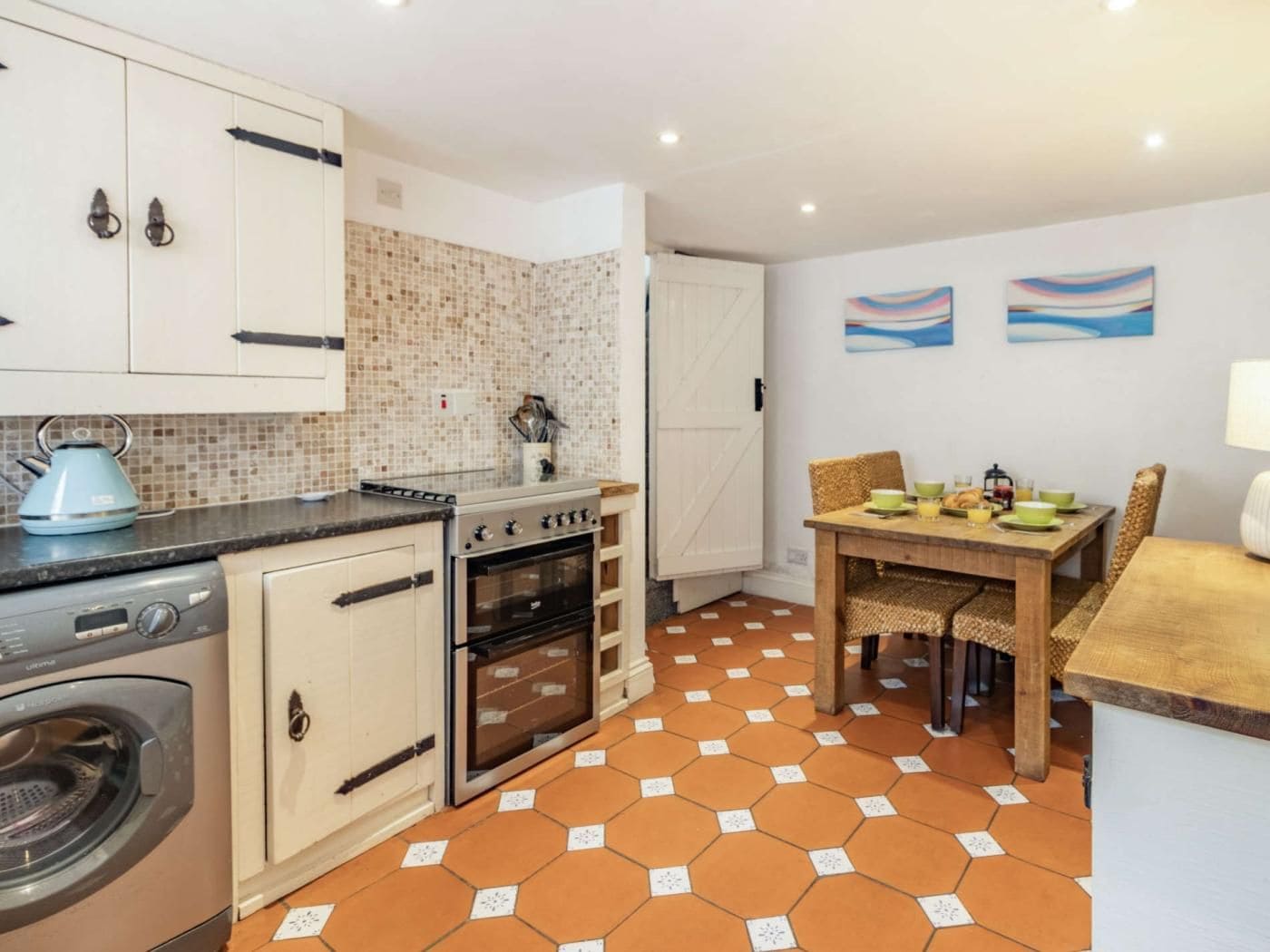 A compact kitchen with a washing machine, a stove, and an oven. There is a dining area with a table and chairs.