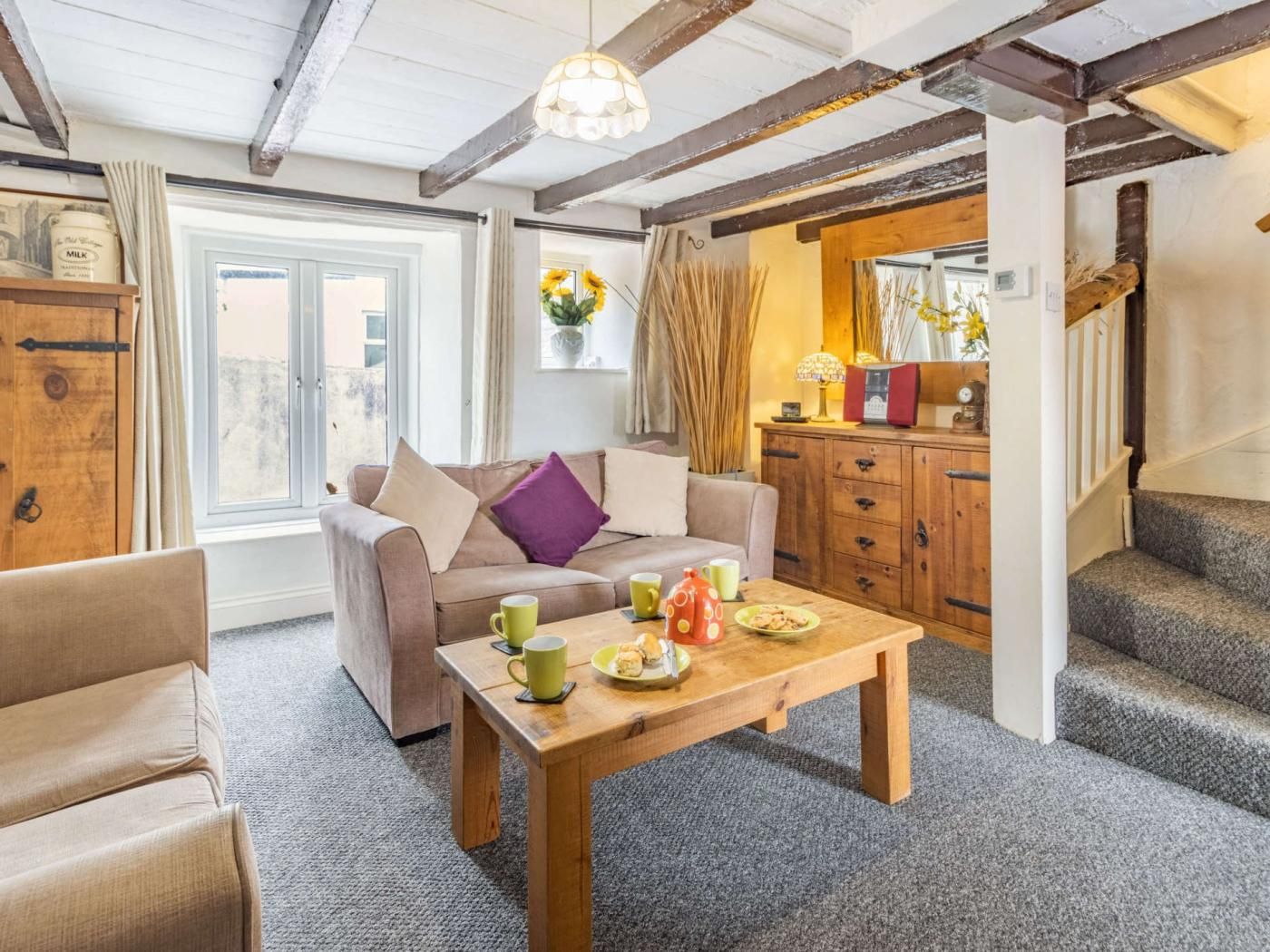 A cozy living room with a sofa, a coffee table with breakfast items, and a staircase leading to another room.