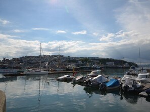 A marina with boats docked, a town in the background, and a clear sky. - 2 Bed in Brixham (oc-88019) (Brixham)