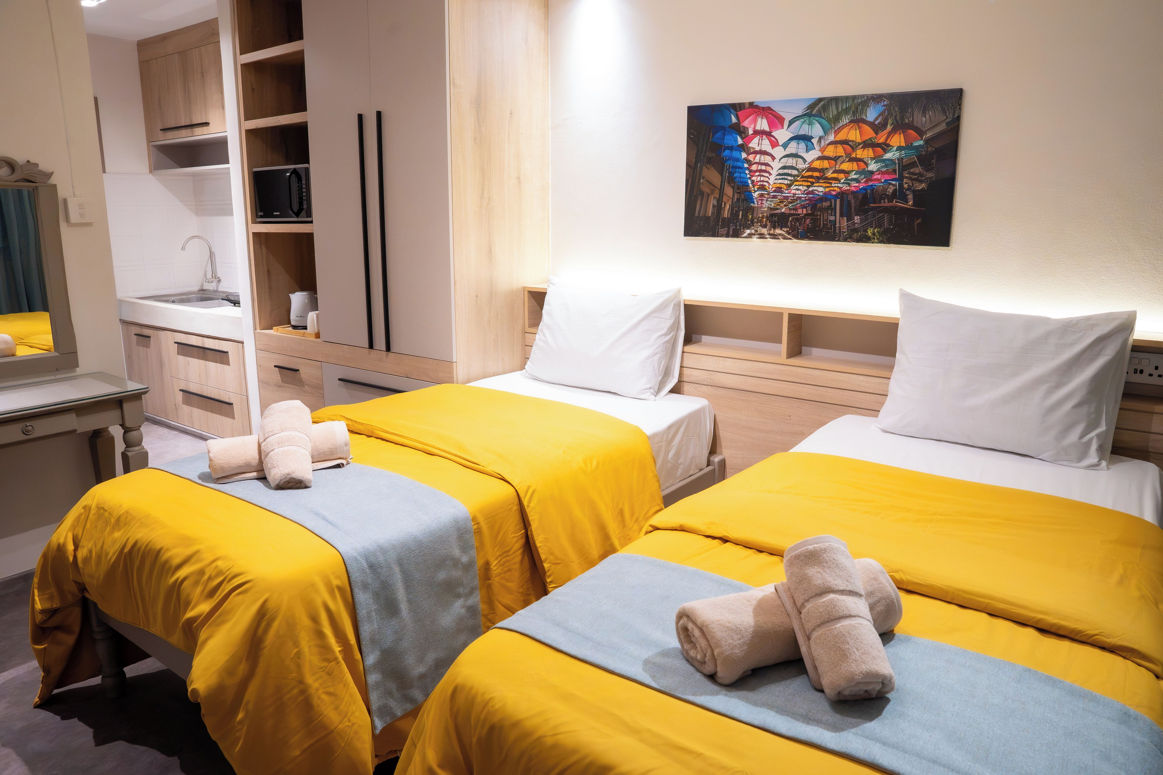 A hotel room with two beds, a kitchenette, and a painting on the wall.