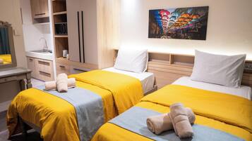 A hotel room with two beds, a kitchenette, and a painting on the wall.