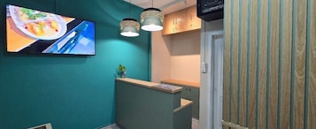 Un área de recepción con pared color verde azulado, mostrador de madera e iluminación colgante.