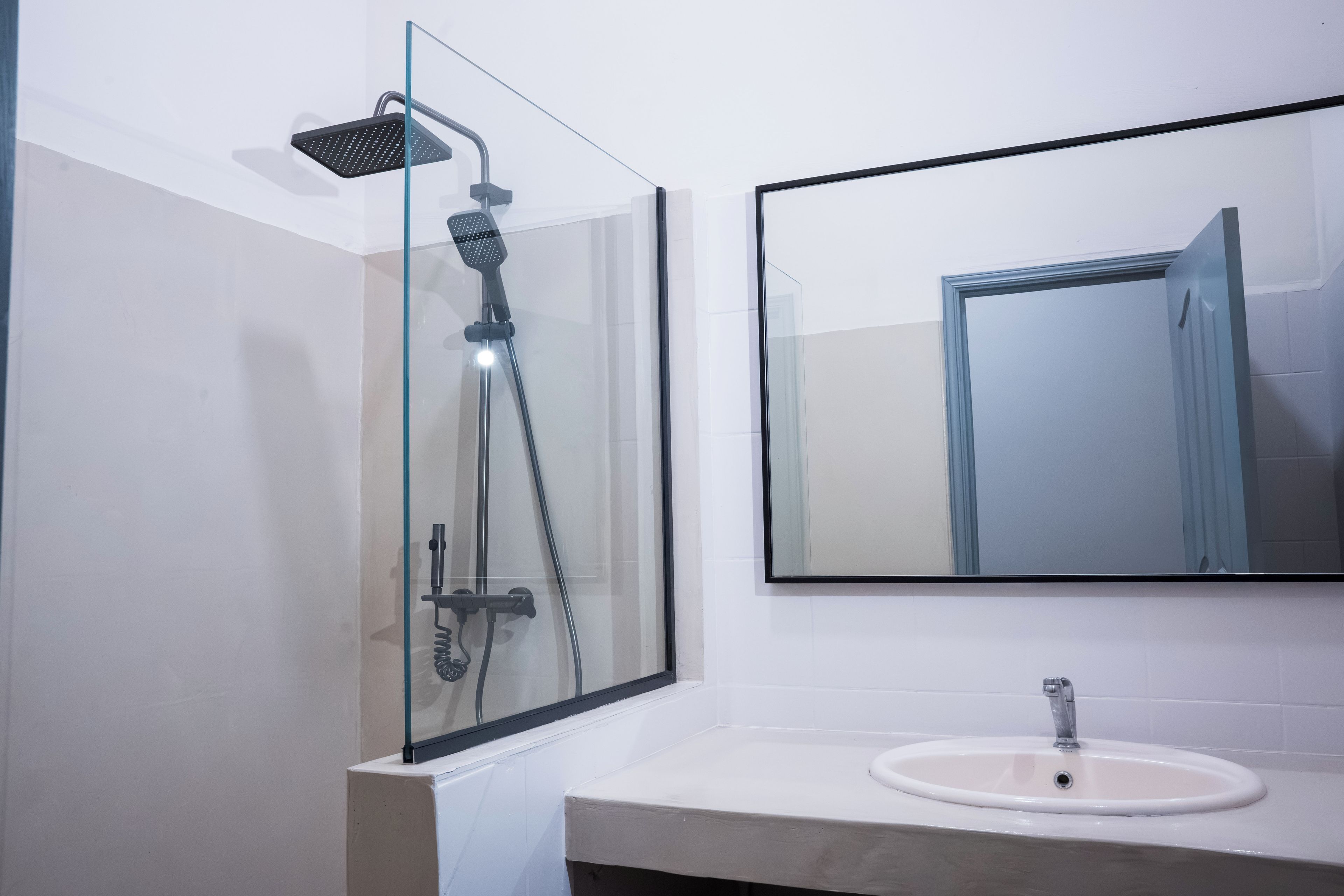 A modern bathroom with a glass-enclosed shower, a white sink, and a large mirror.