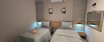 A hotel room with two single beds, a nightstand with a lamp, and a wall-mounted mirror.