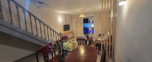 A dining area with a wooden table, chairs, and a vase of flowers. A staircase with a railing is visible to the left.