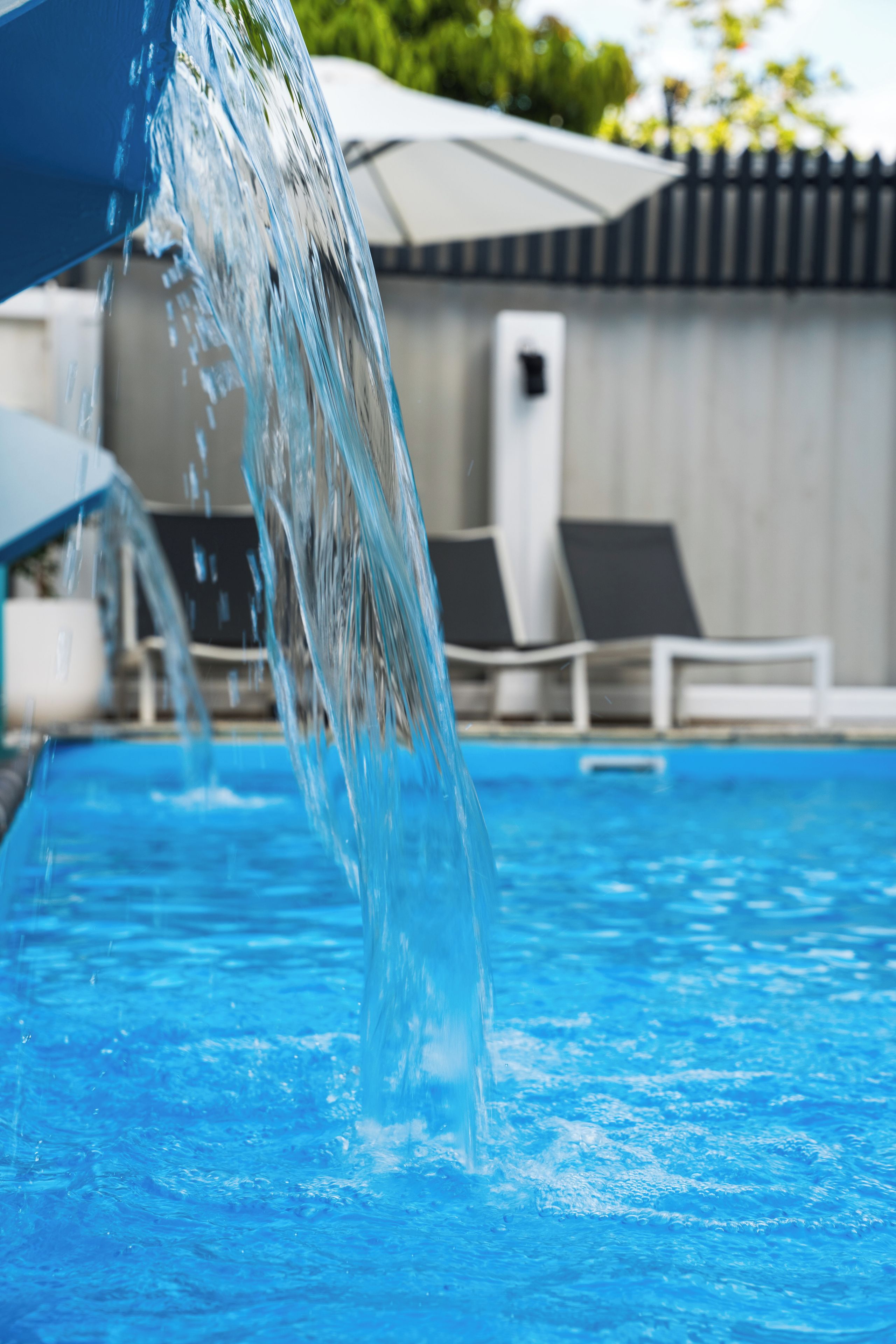 Une piscine avec de l’eau qui jaillit d’une structure, entourée de chaises longues et de parasols.