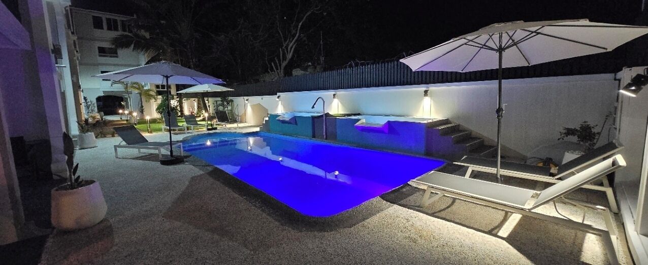 Ein Swimmingpool mit zwei Liegestühlen und Sonnenschirmen, umgeben von einem überdachten Sitzbereich.