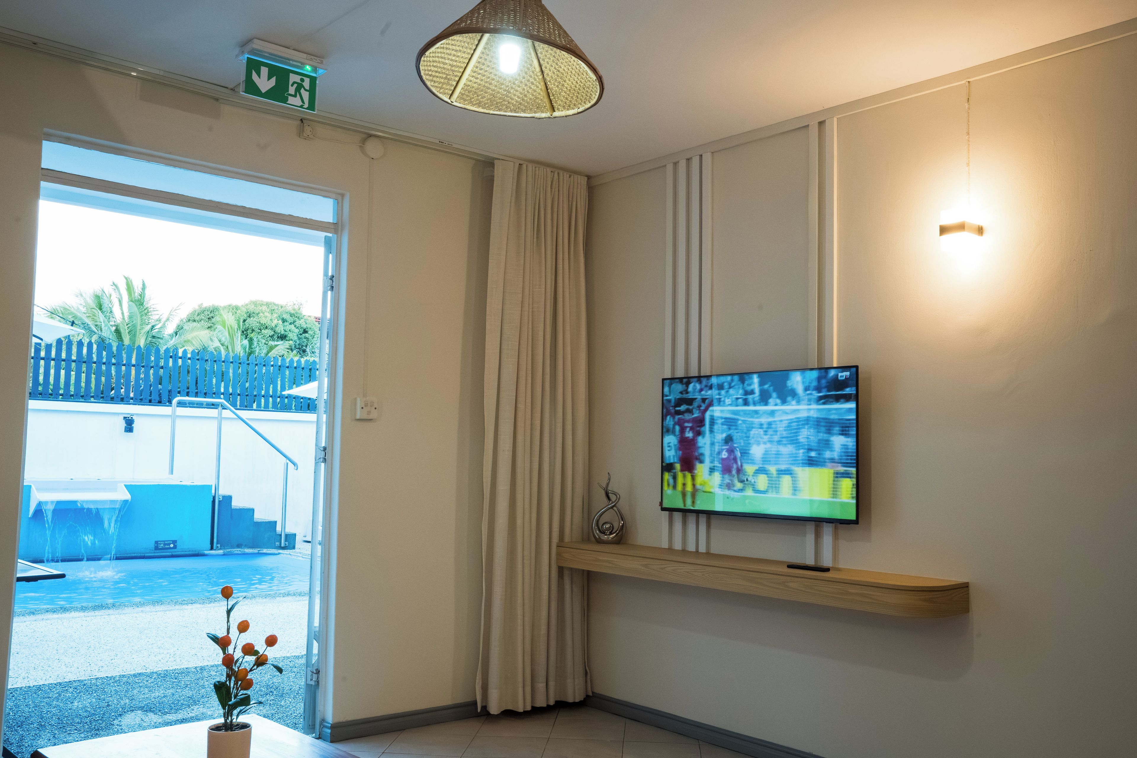 Ein Hotelzimmer mit an der Wand montiertem Fernseher, einer zur Außenseite führenden Tür und einer Deckenleuchte.