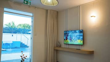 Ein Hotelzimmer mit an der Wand montiertem Fernseher, einer zur Außenseite führenden Tür und einer Deckenleuchte.