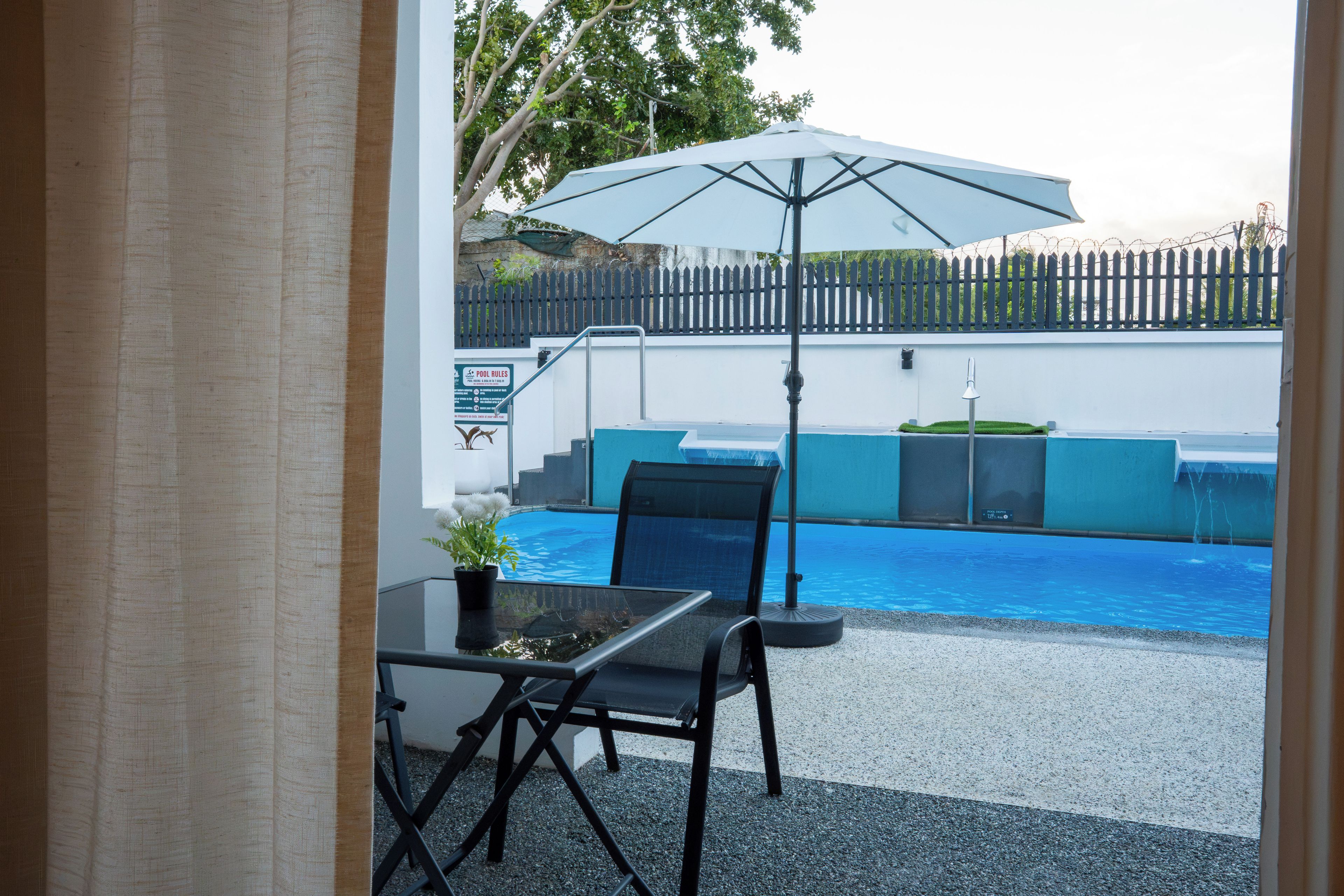 Et poolområde med et bord, stole og en parasol, samt et skilt med information om poolregler.