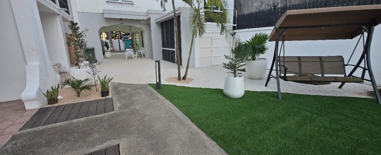 A courtyard with a swing set, a small garden area with potted plants, and a paved walkway leading to a building entrance.