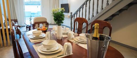 A dining area with a wooden table set for a meal, a metal bucket with a bottle, and a staircase in the background.