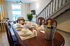 A dining area with a wooden table set for a meal, a metal bucket with a bottle, and a staircase in the background.