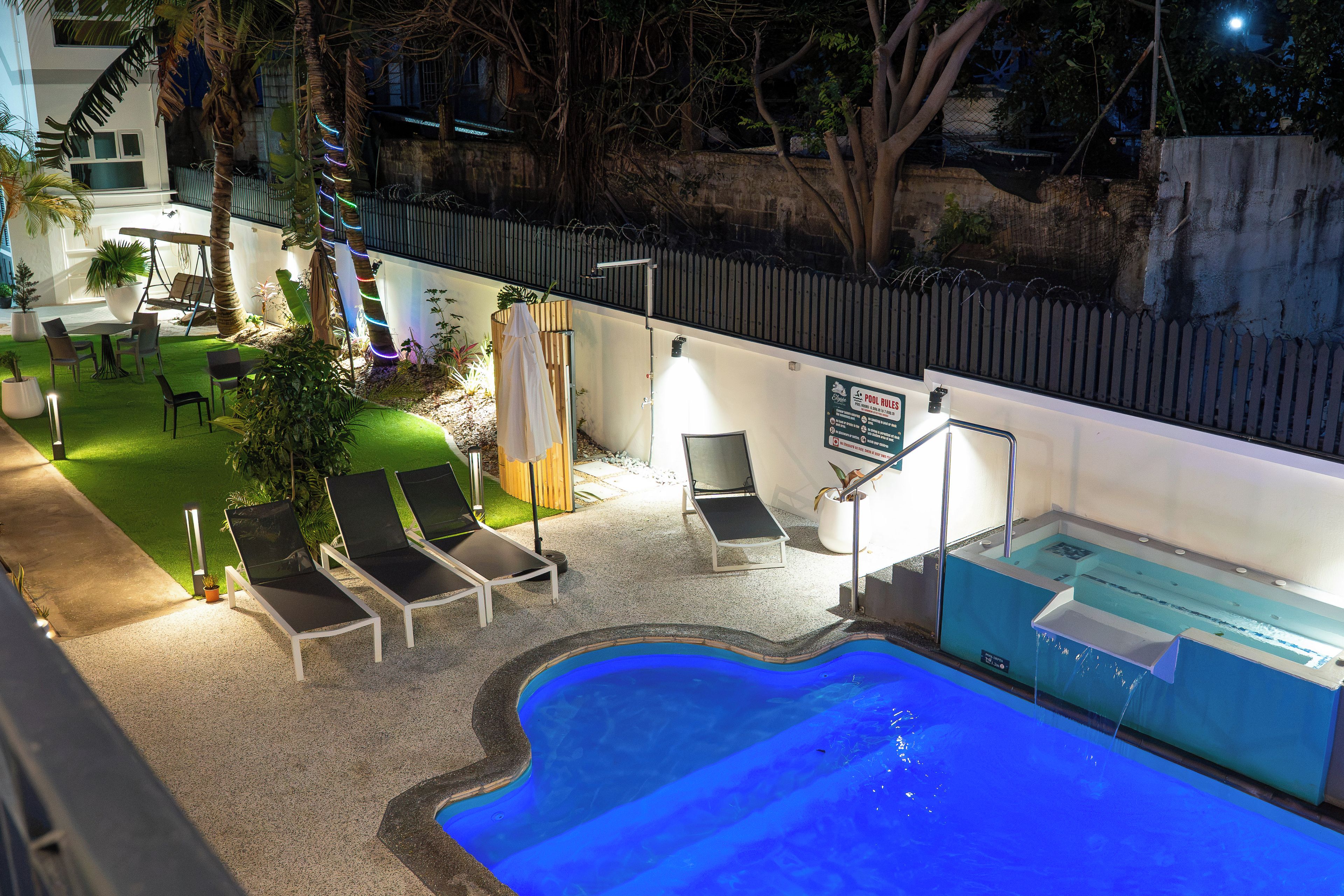 Zona de piscina exterior con sillones de descanso, jacuzzi y jardín vallado.