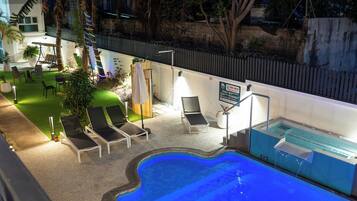 Zona de piscina exterior con sillones de descanso, jacuzzi y jardín vallado.