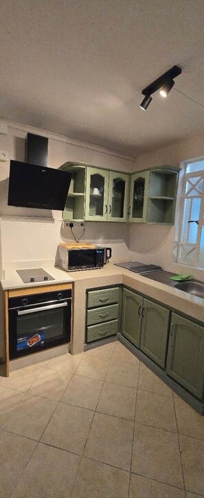 A kitchen with green cabinets, a microwave, a stove, and a window with a view.
