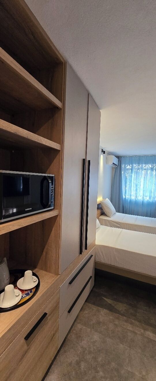 A hotel room with a bed, a microwave, a wooden cabinet, and a window with curtains.