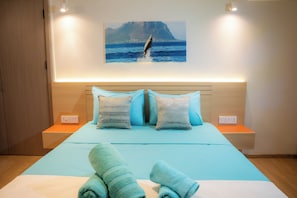 A bed with a blue bedspread, two pillows, and a pair of rolled towels.