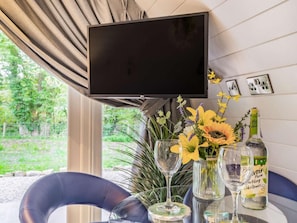 A room with a mounted television, a table with a vase of flowers, a bottle of sparkling wine, and a glass. - 1 Bed in Consett (oc-87933) (Shotley Low Quarter)