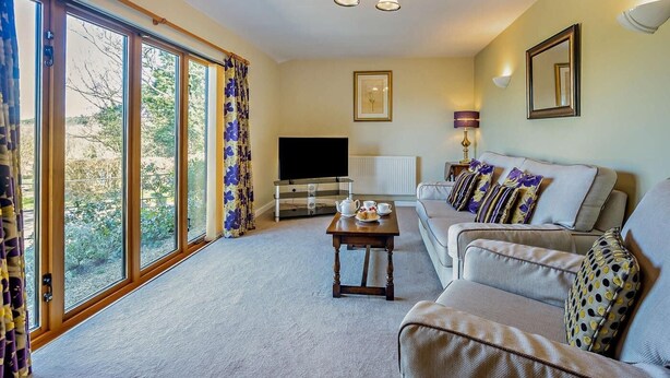 A living room with a sofa, a coffee table, a TV, and a window with curtains. - 2 Bed in Aldham (oc-87956) (Aldham)