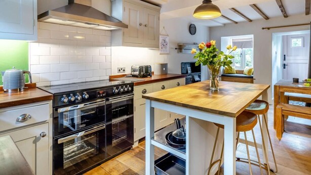 A modern kitchen with white cabinets, a wooden countertop, a built-in oven, and a wooden dining table with bar stools. - 3 Bed in Ulverston (oc-87960) (Penny Bridge)