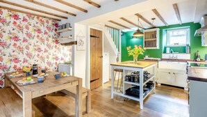 A cozy kitchen with wooden beams, a dining table with breakfast items, and a green accent wall. - 3 Bed in Ulverston (oc-87960) (Penny Bridge)