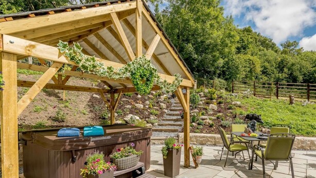 Eine Pergola aus Holz mit Whirlpool, Sitzgelegenheit im Freien und Topfpflanzen.