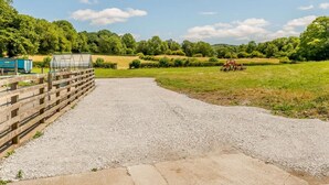 Ein Kiesweg führt zu einem Holzzaun mit einem Gewächshaus und landwirtschaftlichen Geräten.