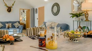 Ein Wohnzimmer mit einer Couch, einem Couchtisch mit einem Glasbehälter, einer Obstschale und einem an der Wand befestigten Hirschkopf.