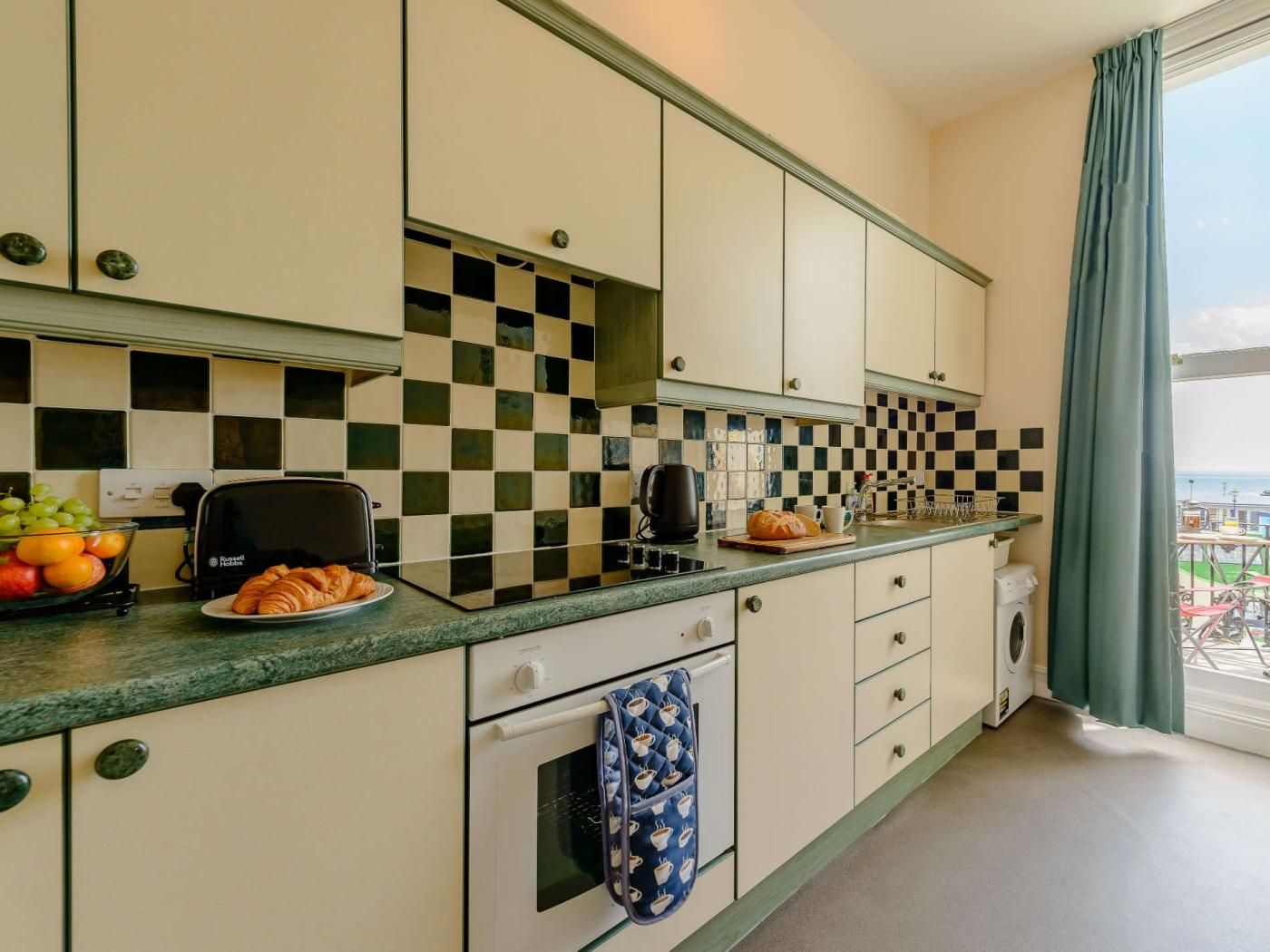 A compact kitchen with a checkered backsplash, a toaster, a bread loaf, and a fruit bowl.