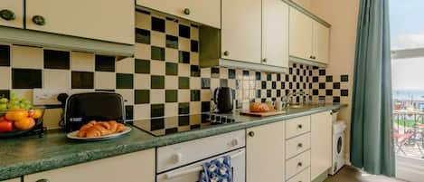 A compact kitchen with a checkered backsplash, a toaster, a bread loaf, and a fruit bowl.