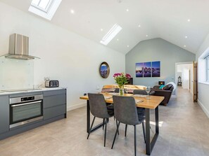 Eine moderne Küche mit Einbauofen, ein Essbereich mit Holztisch und Stühlen sowie ein Wohnbereich mit einer Couch und einem Stadtbild.