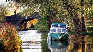 A boat docked at a calm river with a stone bridge in the background.