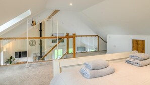 A bedroom with a large bed, a wooden staircase, and a glass wall.