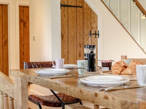 A wooden dining table with plates, a coffee maker, and croissants.