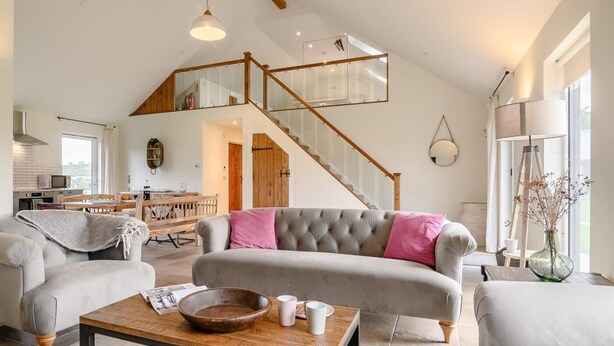 A spacious living area with a high ceiling, a staircase leading to an upper level, a dining area, and a kitchen.