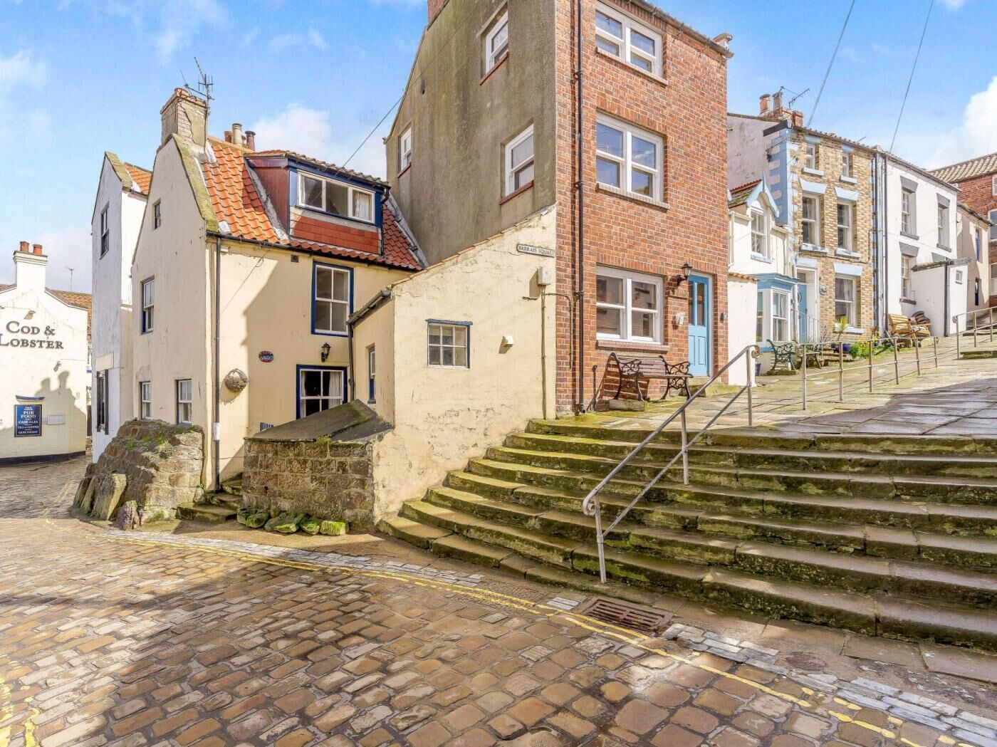 Une rue pavée, avec un bâtiment portant l’inscription « Cod & Lobster » et un escalier menant à un niveau supérieur.