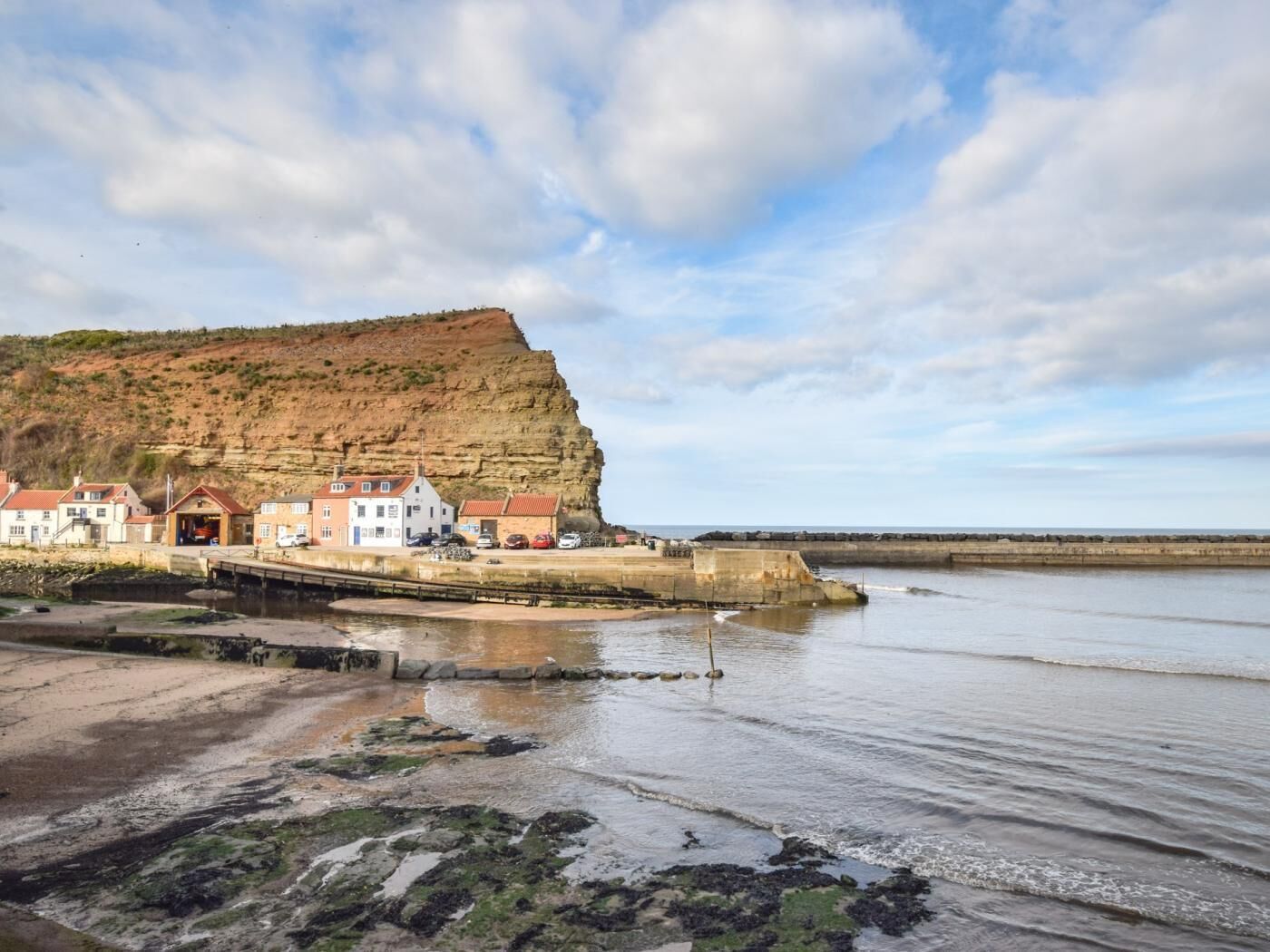 Un pueblo costero con edificios cerca del mar, un acantilado y un muelle.