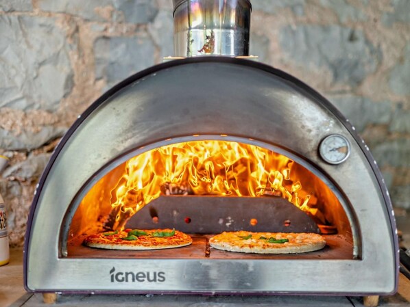 A wood-fired pizza oven with two pizzas inside, branded 'igneus,' set against a stone wall background. - 3 Bed in Ruthin (oc-88123) (Llanbedr-Dyffryn-Clwyd)