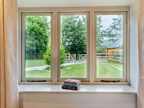 A window with three panes overlooking a grassy area with a wooden fence and a building in the distance. - 3 Bed in Ruthin (oc-88123) (Llanbedr-Dyffryn-Clwyd)