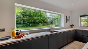 Eine moderne Küche mit einem großen Fenster, dunklen Schränken und einer Arbeitsplatte mit Tellern und einer Obstschale.