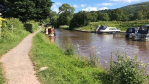 A narrow waterway with boats docked on the right, a dirt path on the left, and lush greenery in the background.