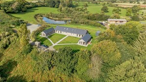 A large, rectangular building with a flat roof, surrounded by green fields and a small pond.