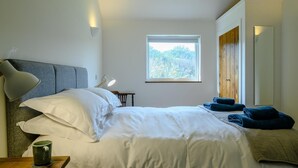 A bedroom with a bed, bedside lamps, a window with a view, and a wooden wardrobe.